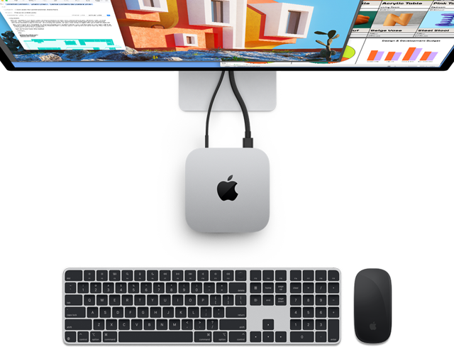 Widok z góry na obudowę Maca mini w kolorze srebrnym z logo Apple. Komputer jest podłączony do monitora, a obok znajdują się bezprzewodowe akcesoria: klawiatura Magic Keyboard i mysz Magic Mouse