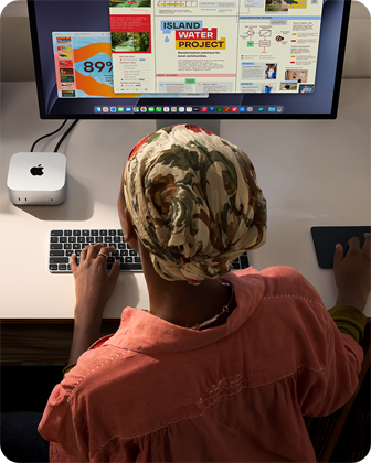 Osoba pisząca przy biurku na Macu mini z podłączonym monitorem Studio Display, klawiaturą Magic Keyboard, gładzikiem Magic Trackpad i różnymi akcesoriami
