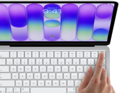 MacBook Neo w kolorze srebrnym z widocznym ekranem logowania i palcem osoby używającej czytnika Touch ID w prawym górnym rogu klawiatury