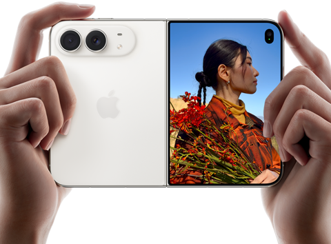Trzymany w dwóch dłoniach rozłożony iPhone Duo w orientacji poziomej, lewy panel przedstawia aparaty tylne Fusion 48 MP, po prawej stronie na wyświetlaczu zewnętrznym widać osobę pozującą do zdjęcia, widzi ona swoją twarz podczas robienia zdjęcia dzięki funkcji Duo Preview