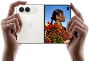 Trzymany w dwóch dłoniach rozłożony iPhone Duo w orientacji poziomej, lewy panel przedstawia aparaty tylne Fusion 48 MP, po prawej stronie na wyświetlaczu zewnętrznym widać osobę pozującą do zdjęcia, widzi ona swoją twarz podczas robienia zdjęcia dzięki funkcji Duo Preview