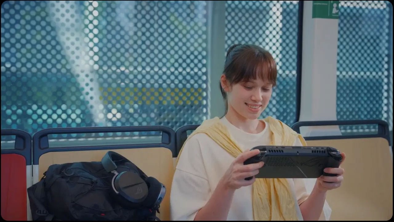 Uśmiechnięta osoba, która siedzi w pociągu i gra na ROG Xbox Ally X.