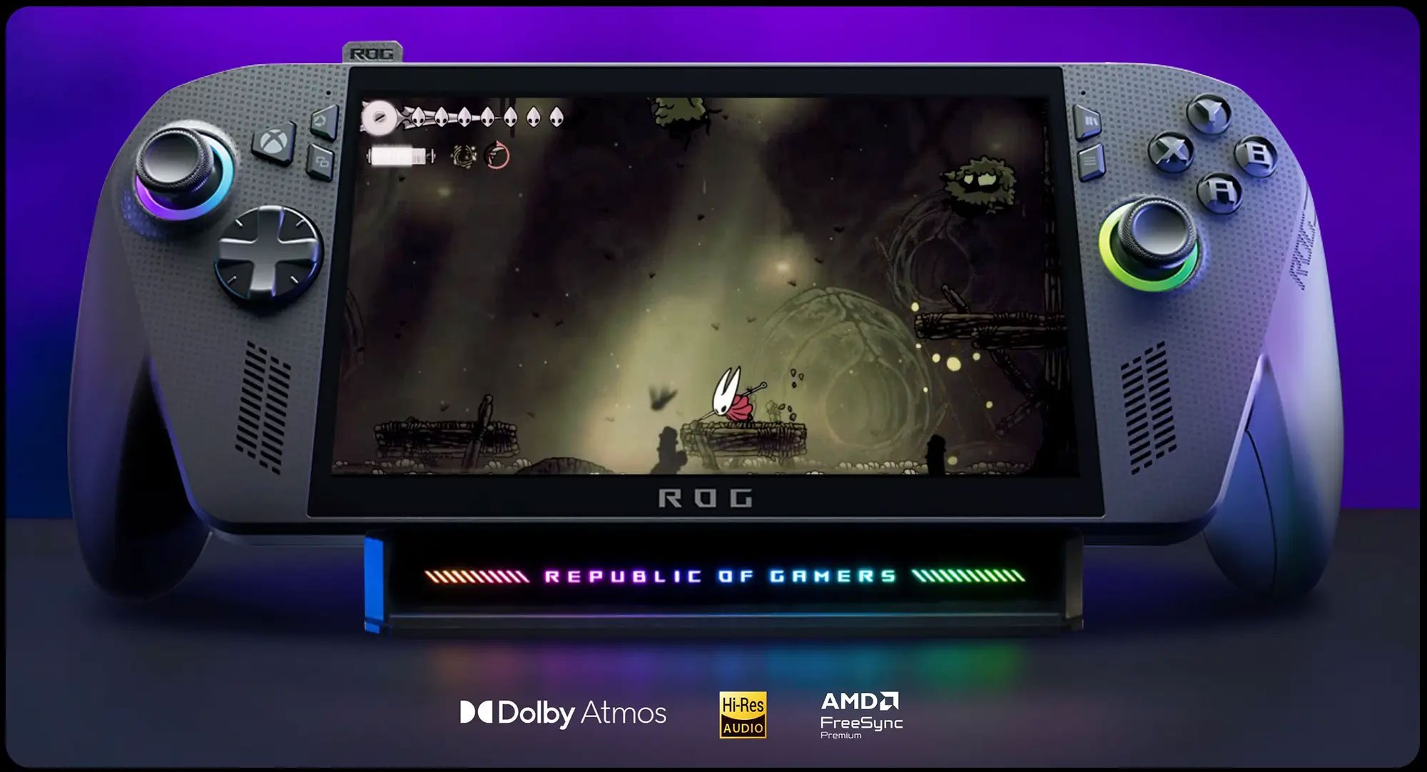 Na zdjęciu widać z bliska ROG Xbox Ally X, leżącą na podstawce, z aktywną grą na ekranie. Pod urządzeniem widoczne są logotypy Dolby Atmos, Hi-Res Audio i AMD FreeSync Premium.