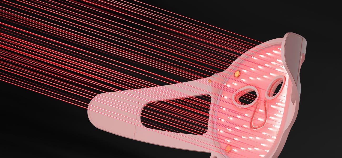 Grafika przedstawiająca jasnoróżową maskę do terapii światłem LED na twarz Beautifly Aura Glam Pro z widocznymi diodami emitującymi czerwone światło, na czarnym tle z czerwonymi liniami świetlnymi