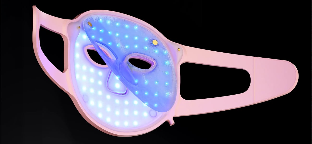Grafika przedstawiająca jasnoróżową maskę do terapii światłem LED na twarz Beautifly Aura Glam Pro z niebieskim podświetleniem diod oraz częściowo odchylonym półprzezroczystym żelowym kompresem chłodzącym na czarnym tle