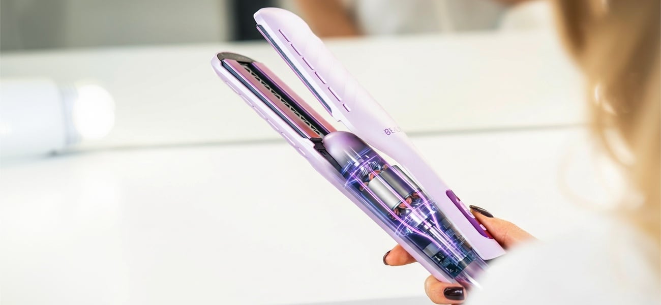 Dłoń trzymająca otwartą aeroprostownicę Beautifly DualPerfection z widocznym wnętrzem urządzenia przedstawiającym elementy mechanizmu i płytki prostujące na jasnym, rozmytym tle