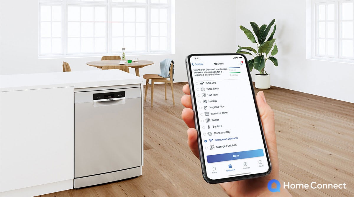 Ręka trzymająca smartfon, na nim aplikacja Home Connect z wyborem trybu pracy zmywarki. w tle Zmywarka marki Bosch.