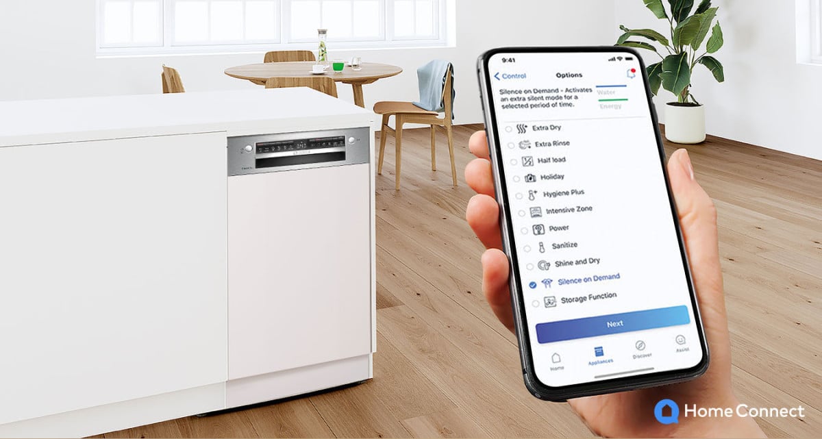 Ręka trzymająca smartfon, na nim aplikacja Home Connect z wyborem trybu pracy zmywarki. w tle Zmywarka marki Bosch