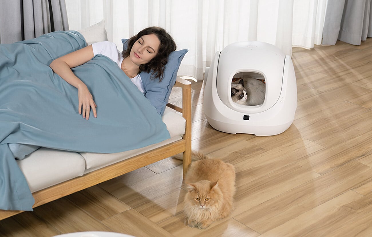Kobieta odpoczywa na łóżku, obok stoi kuweta CATLINK BayMax z kotem w środku
