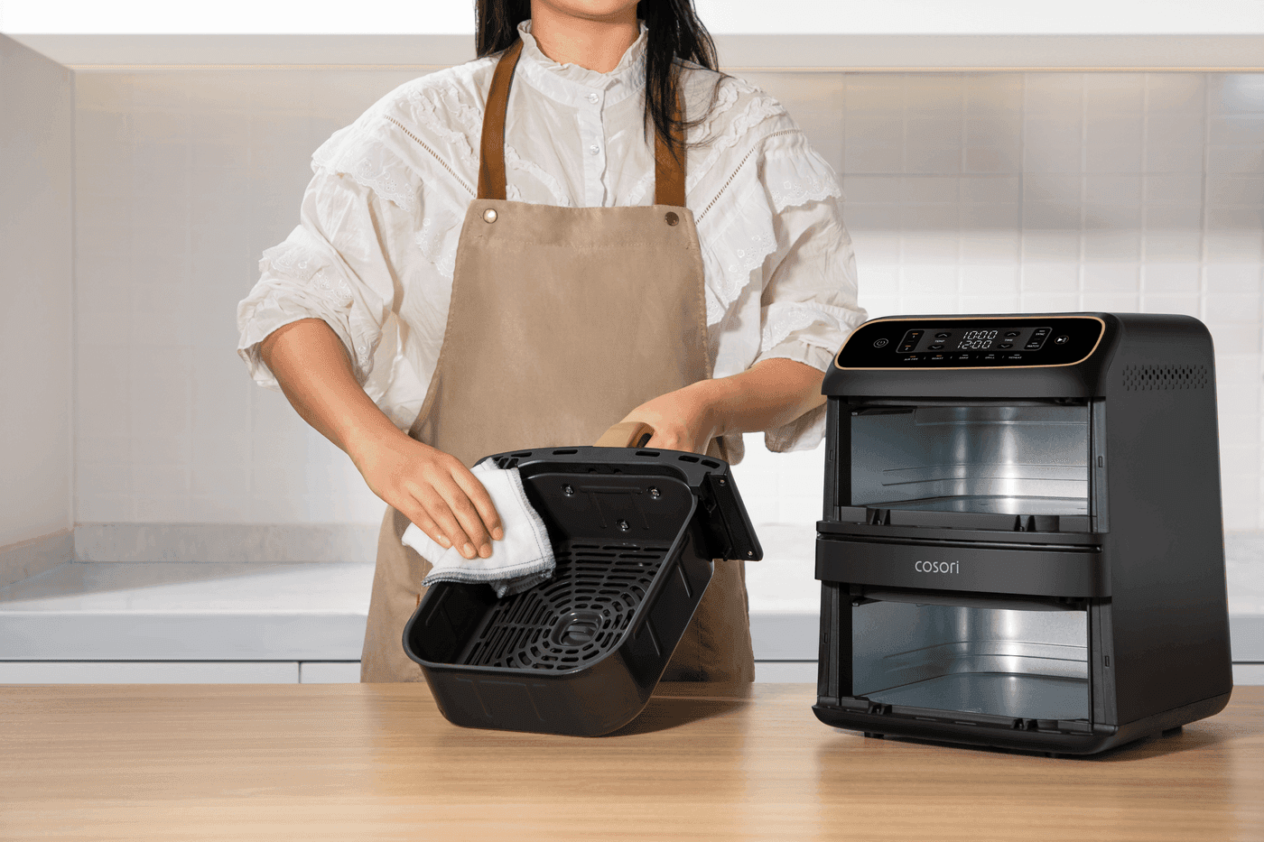 Kobieta w fartuchu przeciera ściereczką wyjęty kosz czarnej frytkownicy Cosori Turbo Tower Compact