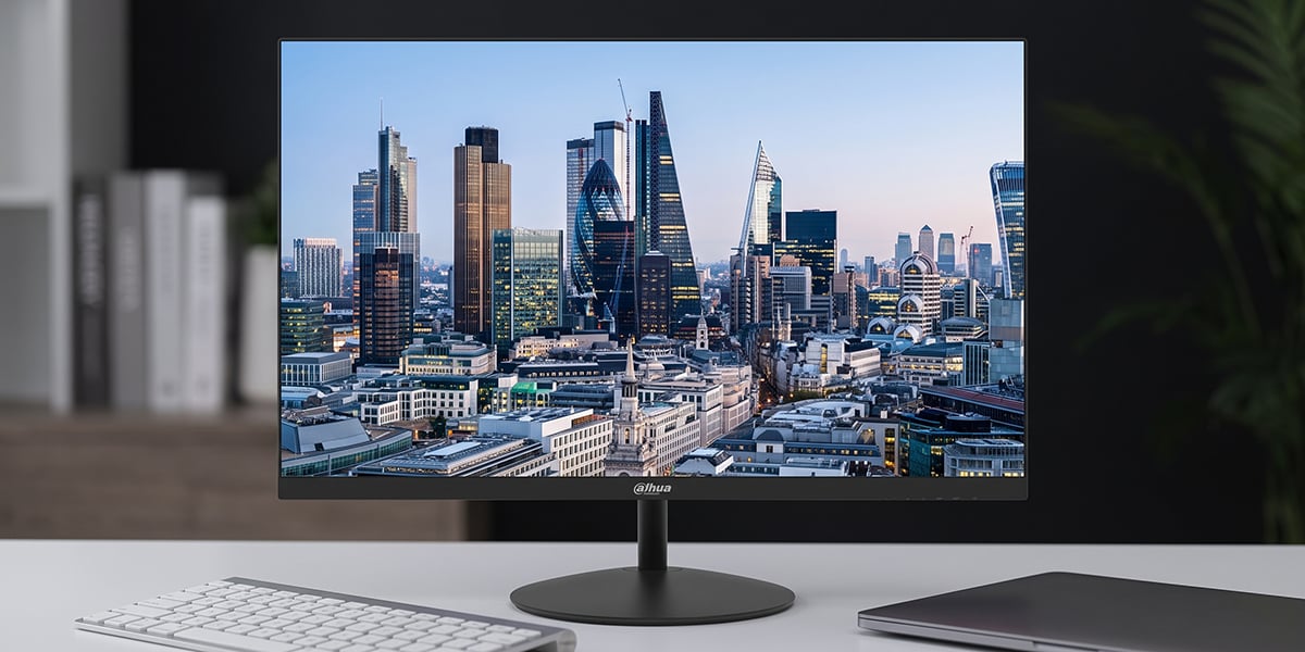 Monitor Dahua stoi na biurku na okrągłej podstawie i wyświetla panoramę nowoczesnego miasta o zmierzchu