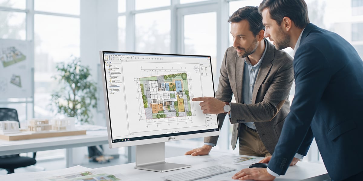 Dwóch mężczyzn w garniturach analizuje plan architektoniczny wyświetlany na ekranie monitora Dahua