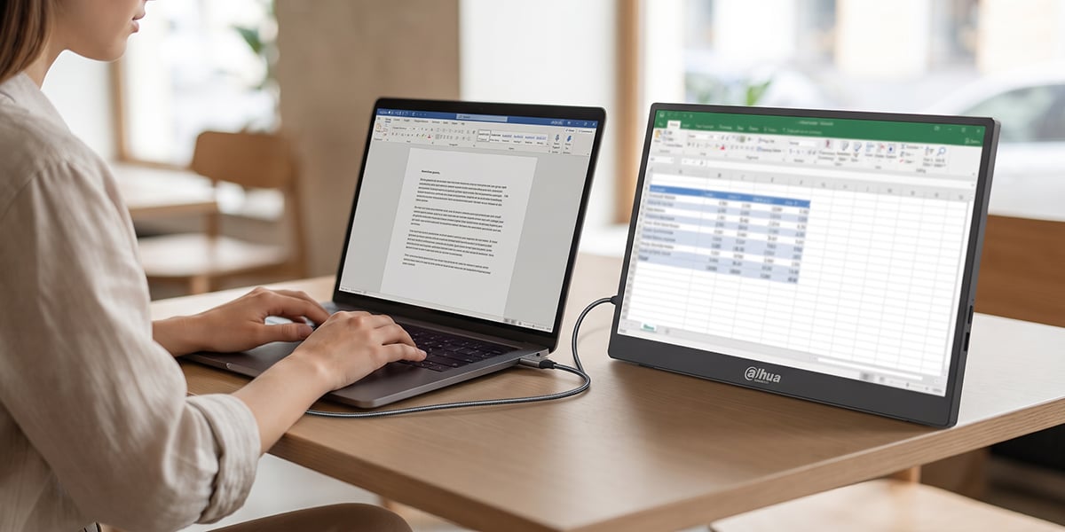 Kobieta pisze na laptopie połączonym z monitorem Dahua, na którym widać otwarty arkusz kalkulacyjny