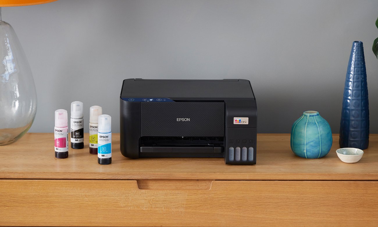 Epson EcoTank L3211 ustawiona na biurku, obok znajdują się tusze