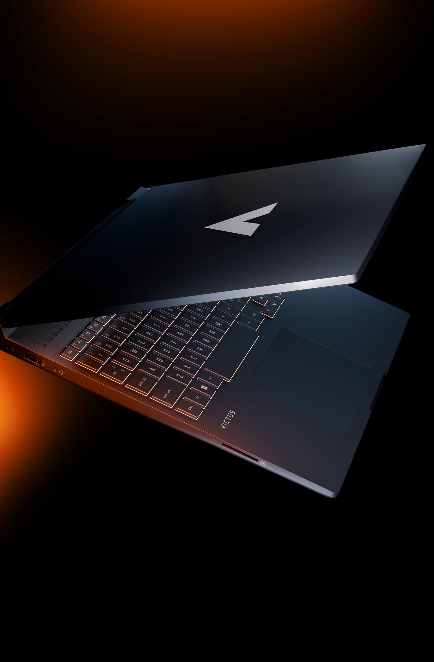 Zbliżenie na lekko otwartą obudowę laptopa HP Victus, prezentujące podświetlaną na pomarańczowo klawiaturę oraz logo serii na pokrywie.