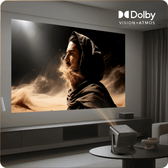 Projektor na stoliku wyświetlający postać w kapturze na ścianie oraz logo Dolby VISION i ATMOS u góry.