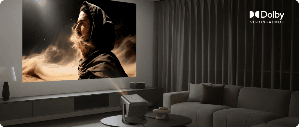 Projektor na stoliku wyświetlający postać w kapturze na ścianie oraz logo Dolby VISION i ATMOS u góry.
