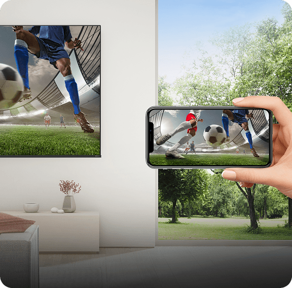 Ręka trzyma smartfon wyświetlający mecz piłki nożnej, przesyłając obraz na duży ekran telewizora w salonie