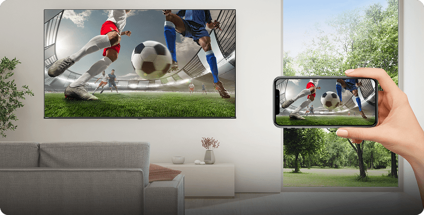 Ręka trzyma smartfon wyświetlający mecz piłki nożnej, przesyłając obraz na duży ekran telewizora w salonie