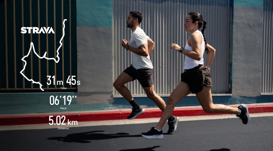 Dwie osoby biegające po miejskiej ulicy z nałożoną grafiką statystyk i trasy z aplikacji Strava.