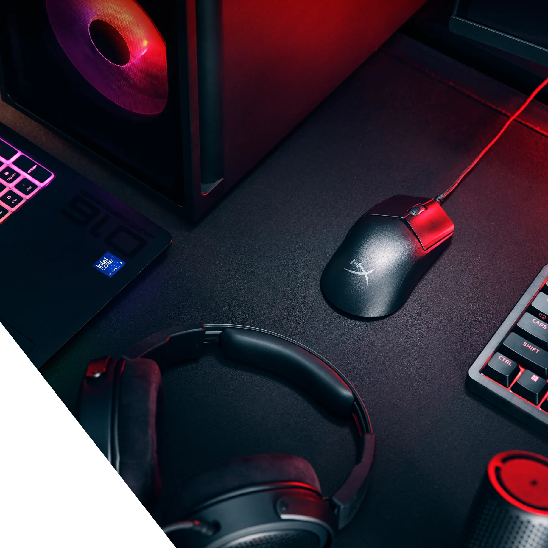 Czarna mysz HyperX z przewodem na podkładce między komputerem, laptopem, słuchawkami i klawiaturą w czerwonym świetle