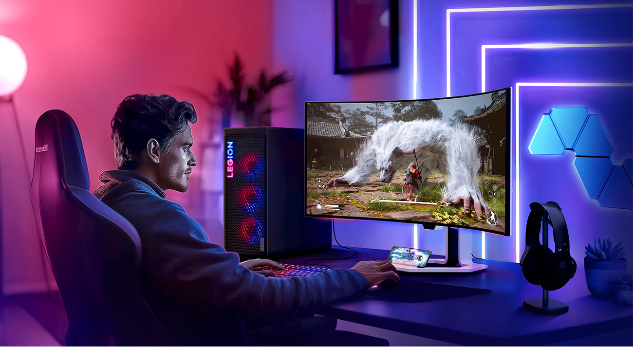 Monitor Lenovo Legion Pro 34WD-10 na biurku przed którym siedzi młoda osoba i gra w grę komputerową