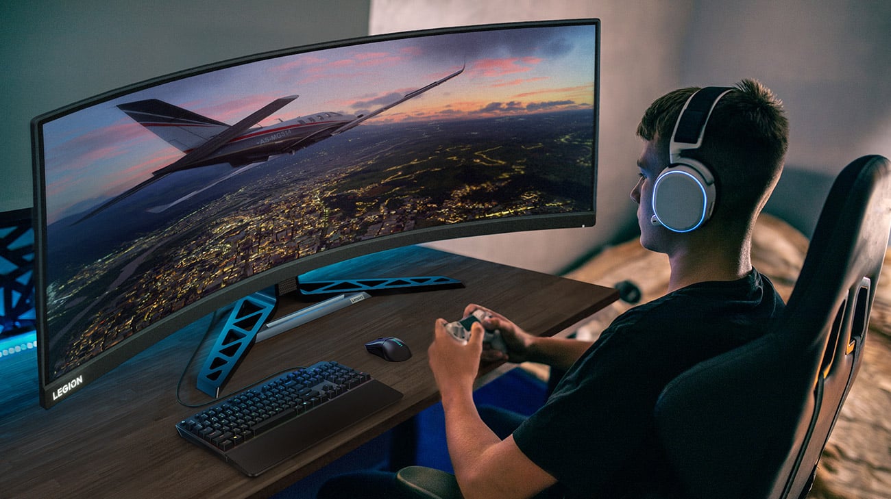 Monitor Lenovo R45w-30 na biurku przed którym siedzi młoda osoba ze słuchawkami na głowie i gra w grę komputerową