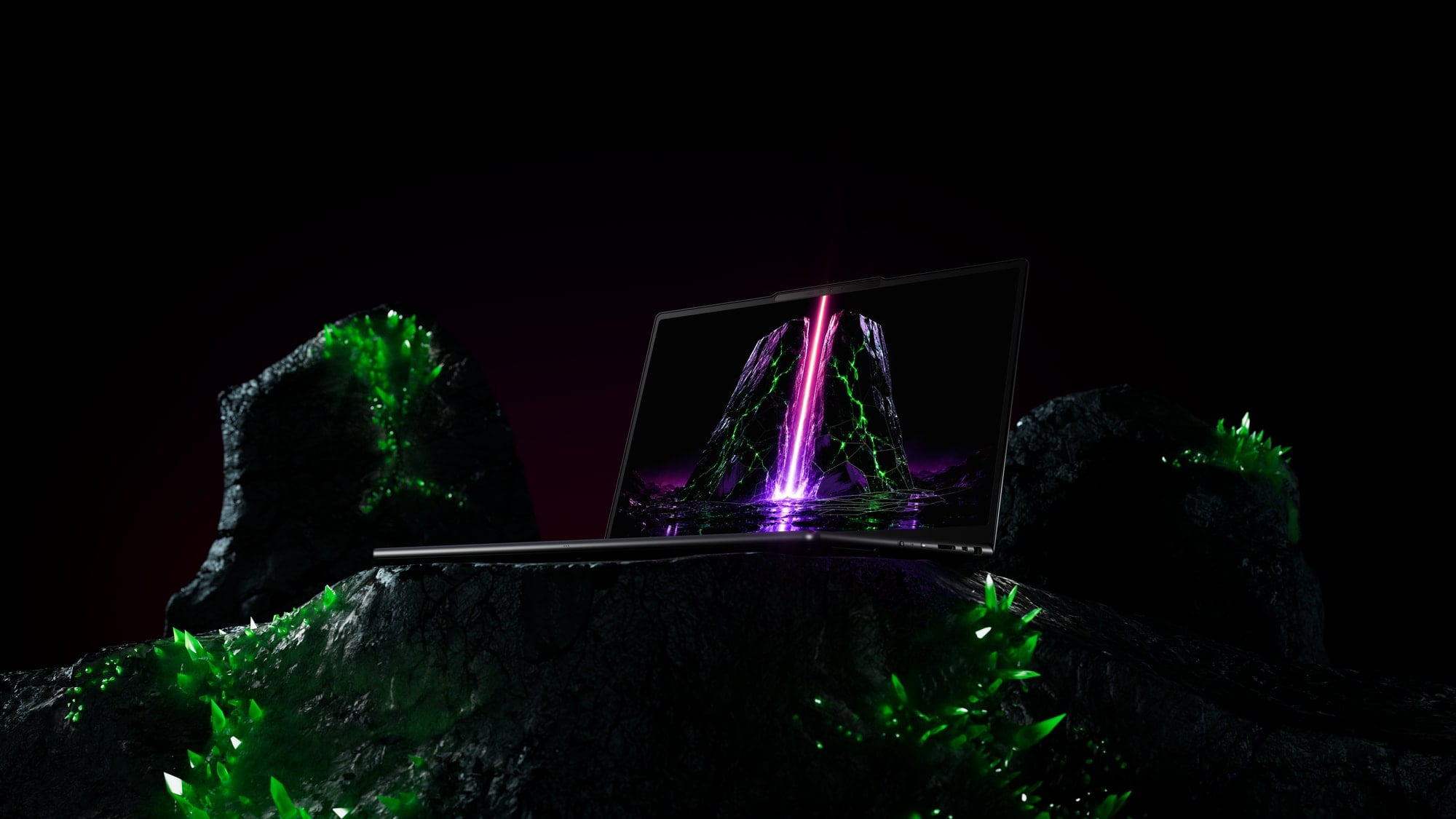 Laptop umieszczony na ciemnej skale z zielonymi kryształami w mrocznej, neonowej scenerii.