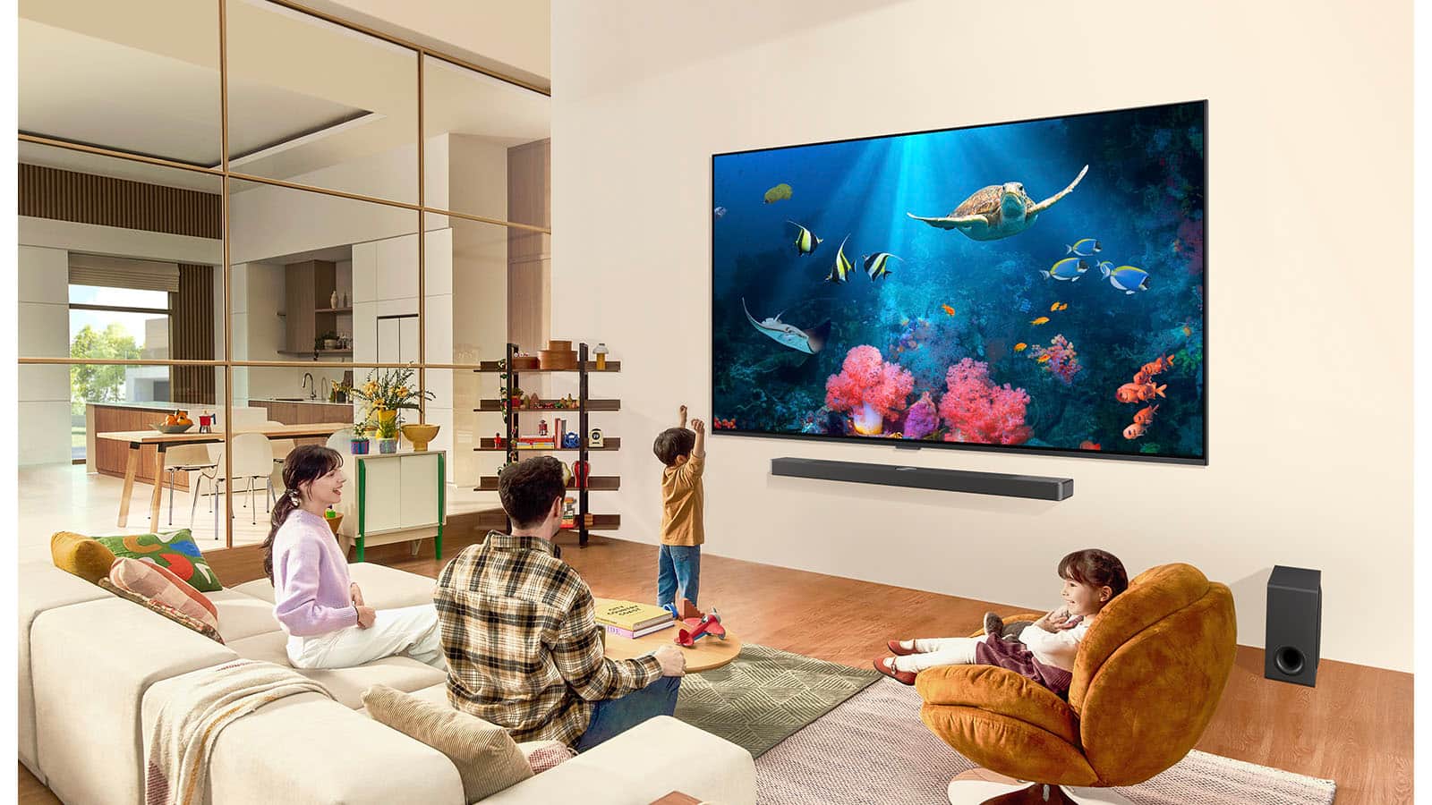 Rodzina będąca w salonie z bardzo dużym telewizorem LG, zamontowanym na ścianie, ze sceną oceanu z koralowcami i żółwiem na ekranie.