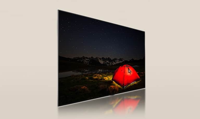 Telewizor LG z przyciemnionym ekranem, wyświetlający ciemną noc i jaskrawoczerwony namiot. Niebieski panel podświetlenia zostaje podzielony z tyłu telewizora. Małe bloki przyciemniające rozproszone są po całym panelu. Następnie panel i telewizor są łączone, aby ekran był jaśniejszy i wyraźniejszy.