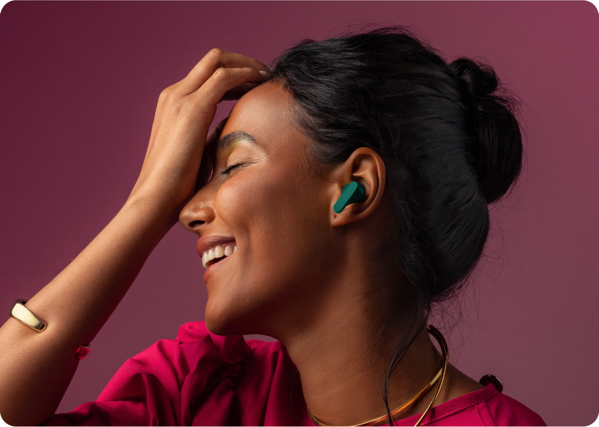 Uśmiechnięta kobieta z zamkniętymi oczami, mająca w uchu zieloną słuchawkę bezprzewodową