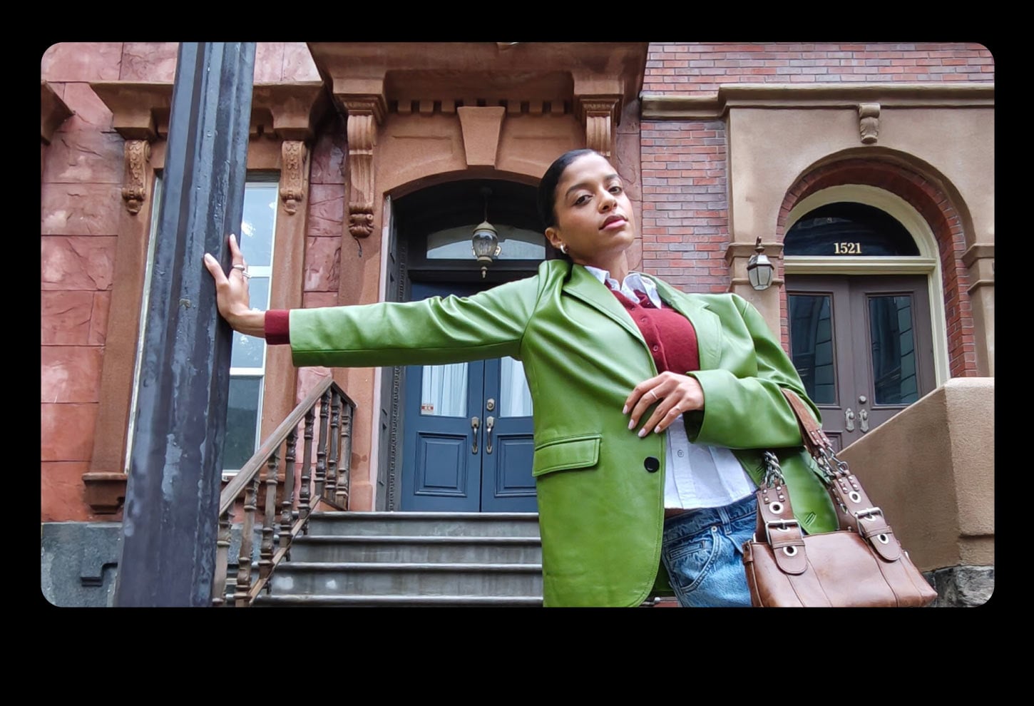 Kobieta w zielonej marynarce na tle kamienicy, uchwycona szerokokątnym obiektywem