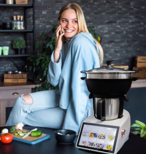 Termorobot iCoook 3.0 Plus na kuchennym blacie. Obok kobieta zagląda do garnka.
