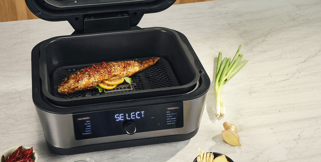 Multicooker z napisem SELECT na panelu, pieczona ryba wewnątrz, obok imbir, szczypiorek i papryczki