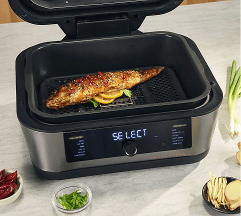 Multicooker z napisem SELECT na panelu, pieczona ryba wewnątrz, obok imbir, szczypiorek i papryczki