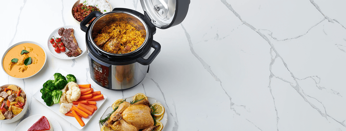 Otwarty multicooker z potrawą z ryżu w środku, otoczony miskami i talerzami z kurczakiem, warzywami oraz gulaszem