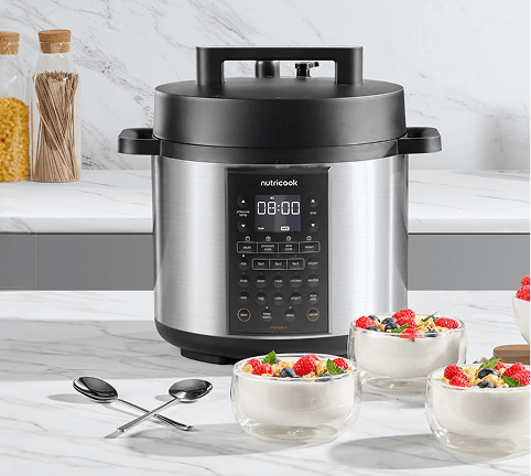 Srebrny multicooker z czarną pokrywą stojący na blacie kuchennym obok trzech szklanych salzerek z deserem z malinami