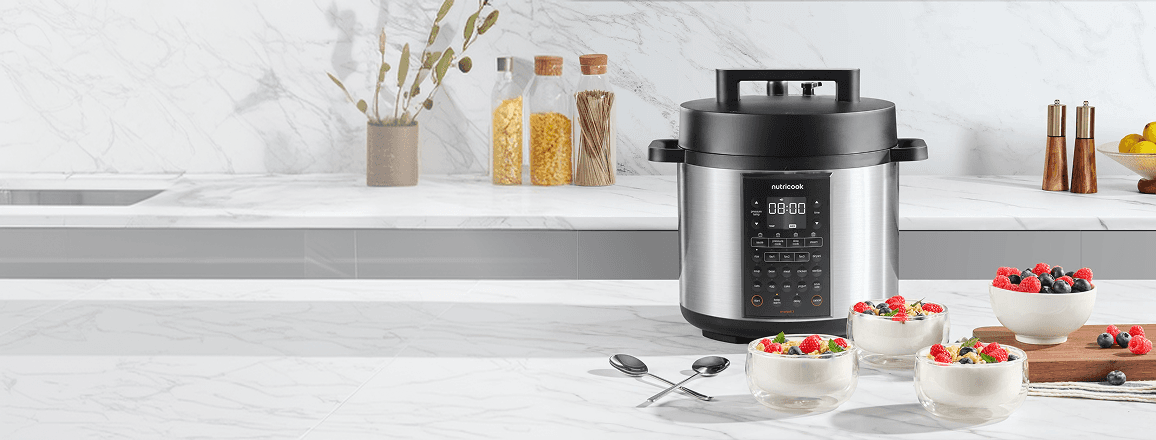 Srebrny multicooker z czarną pokrywą stojący na blacie kuchennym obok trzech szklanych salzerek z deserem z malinami