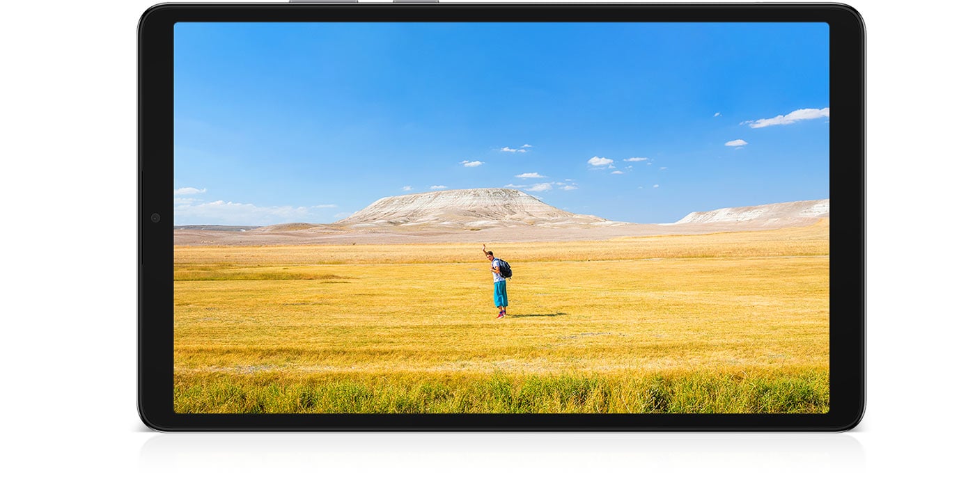 Galaxy Tab A11 jest umieszczony poziomo, wyświetlając wyraźny obraz mężczyzny machającego rękami, co sugeruje swobodny nastrój. W tle błękitne niebo rozciąga się nad szerokim horyzontem żółto-brązowej trawy. Pod tabletem znajduje się napis „Częstotliwość odświeżania 90 Hz”.