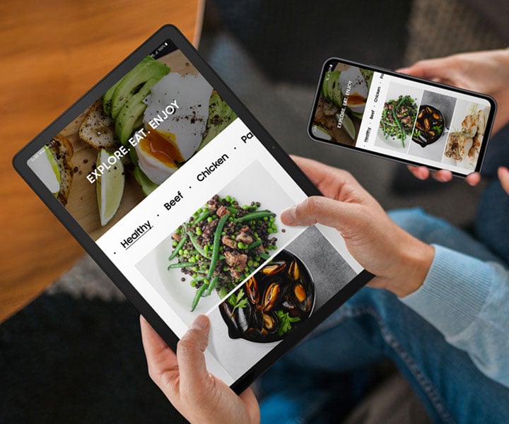 Dwie osoby siedzą obok siebie. Osoba po lewej trzyma Galaxy Tab A9 Plus, a osoba po prawej trzyma smartfon Galaxy. Oba urządzenia wyświetlają tę samą stronę internetową o jedzeniu. Dwie osoby siedzą obok siebie. Osoba po lewej trzyma Galaxy Tab A9 Plus, a osoba po prawej trzyma smartfon Galaxy. Oba urządzenia wyświetlają tę samą stronę internetową o jedzeniu.