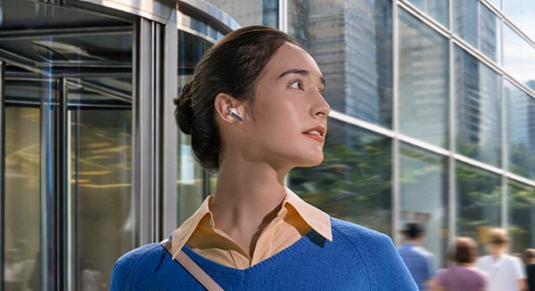 Kobieta z jedną, białą słuchawką Galaxy Buds 4 w uchu, patrząca w prawo przed budynkiem.