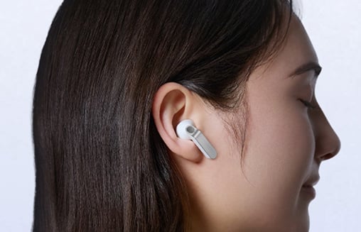 Zbliżenie białych Galaxy Buds 4 z metalowymi krawędziami; scena zmiana, osoba w nich patrzy w prawo.