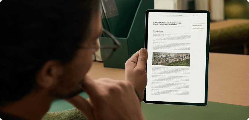 Mężczyzna w okularach trzyma tablet, na którego ekranie wyświetla się artykuł prasowy ze zdjęciem i tekstem.