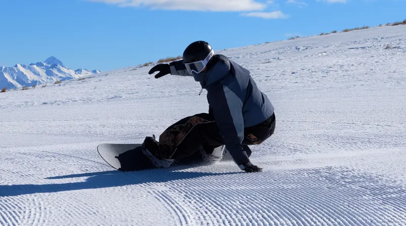 Snowboardzista w szarej kurtce i czarnym kasku skręca na ośnieżonym górskim stoku